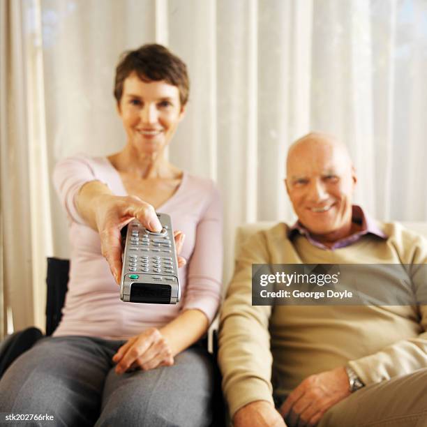 front view portrait of a wife sitting in a wheelchair holding remote control with her husband sitting beside her - control photos et images de collection