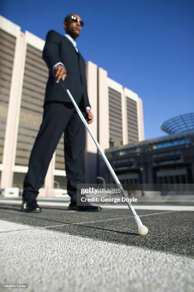 Low Angle View Of A Blind Man Walking With The Aid Of A White