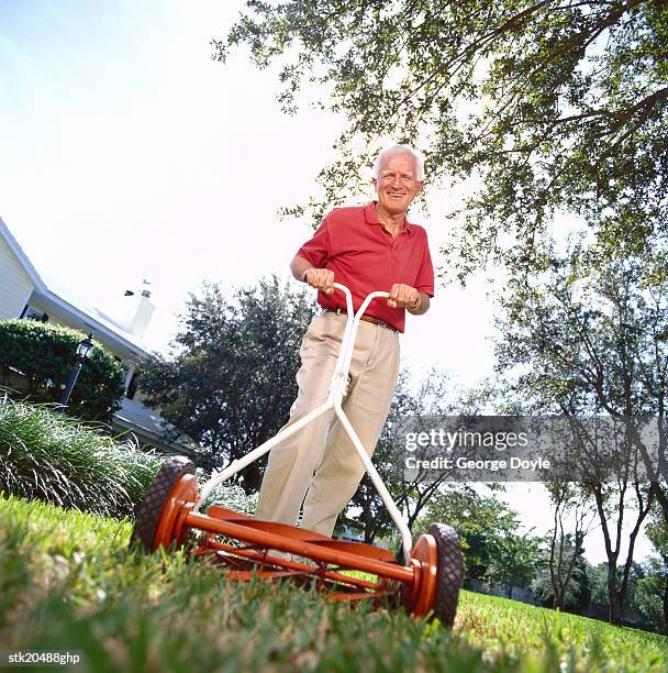 low angle view of an elderly man mowing the lawn with a mower - handgrasmaaier stockfoto's en -beelden