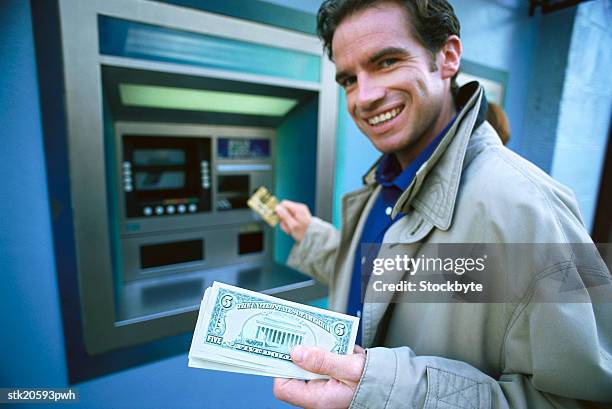 portrait of a young man withdrawing money at an automatic transaction machine - five dollar bill stock pictures, royalty-free photos & images