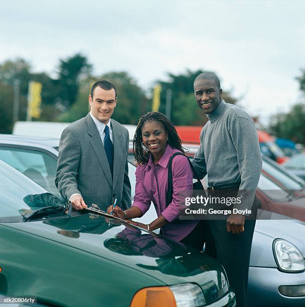 portrait of a young couple signing papers at a car lot - the lot stock-fotos und bilder