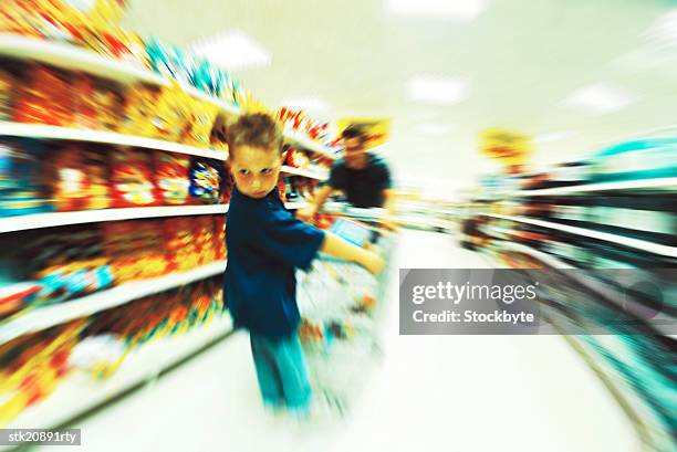 portrait of a young boy (6-10) standing on a shopping cart which is being pushed by his father - is stock pictures, royalty-free photos & images