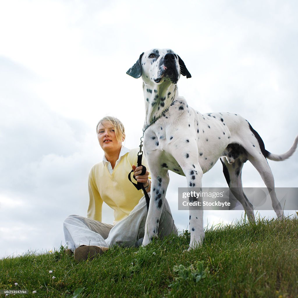 Low angle view of a woman sitting in a field with her Dalmatian dog