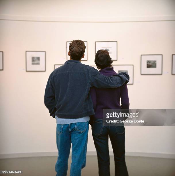 view of a young couple viewing art hung on the wall in a gallery - couple art gallery stock pictures, royalty-free photos & images