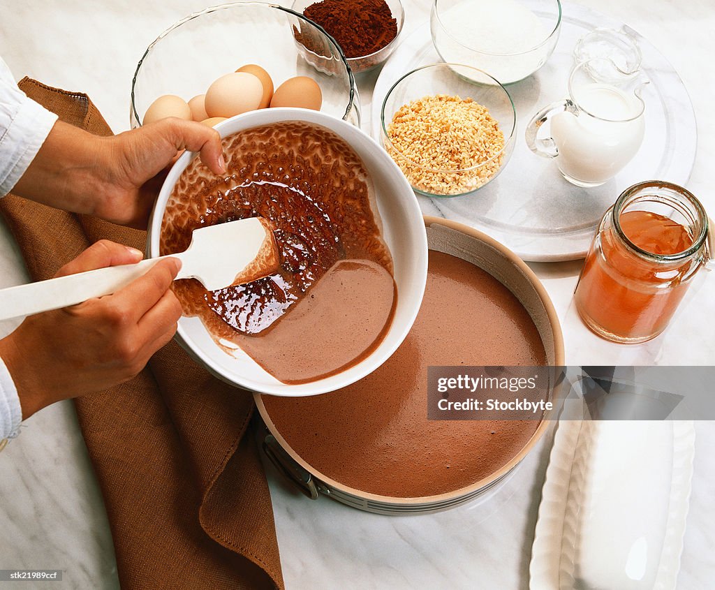 Close-up of hands pouring batter into a baking dish on a table top