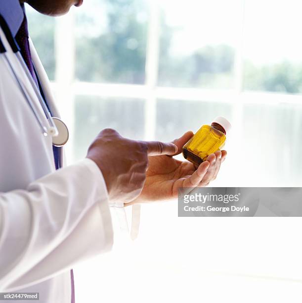 doctor in a lab coat reading the label on a medication bottle - lab coat stock-fotos und bilder