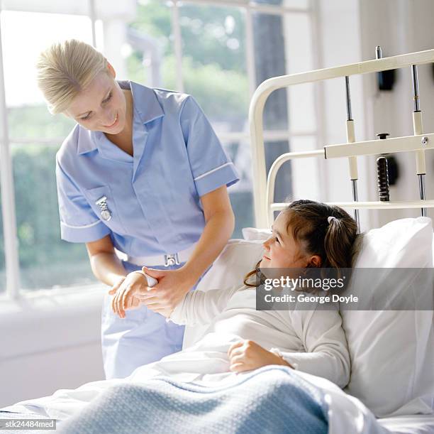 portrait of a young nurse checking the pulse of a little girl in bed - kittle stock-fotos und bilder