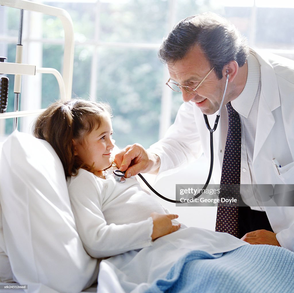 Portrait of a male doctor examining a young girl's chest with a stethoscope