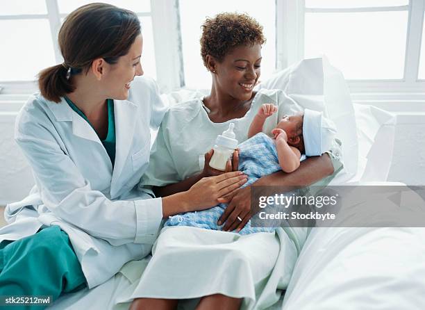 view of a doctor watching a new mother feed the baby with a bottle - nurse with baby stock pictures, royalty-free photos & images