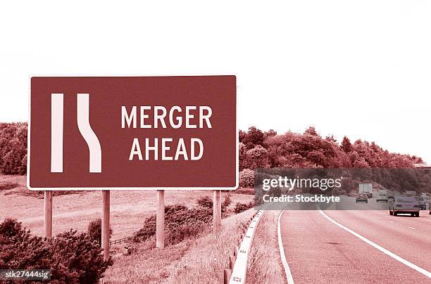 a sepia shot of a road sign saying merger ahead - ahead stock pictures, royalty-free photos & images