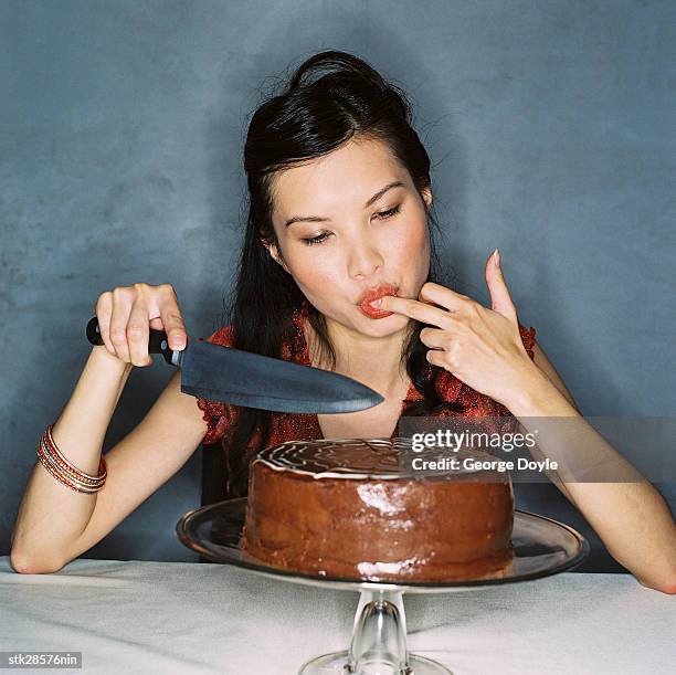 a young woman sitting in front of a chocolate cake with a knife and licking her fingers - taste of john paul ataker presentation spring 2016 new york fashion week stockfoto's en -beelden