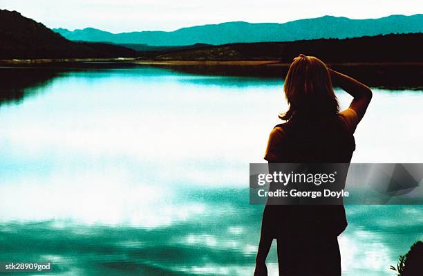 rear view of a young woman looking across a lake - across stock pictures, royalty-free photos & images