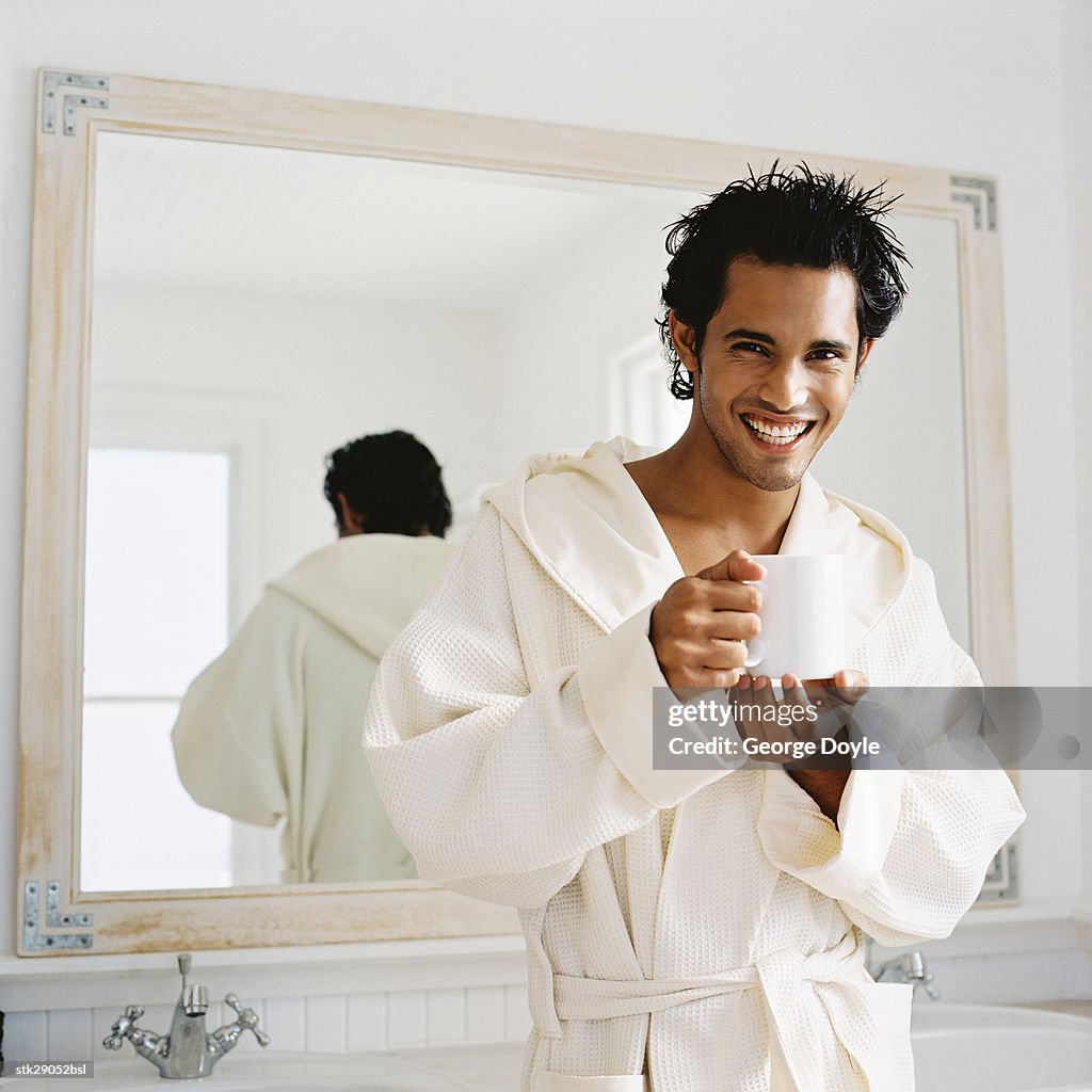 Portrait of a young man standing in a bathrobe holding a mug
