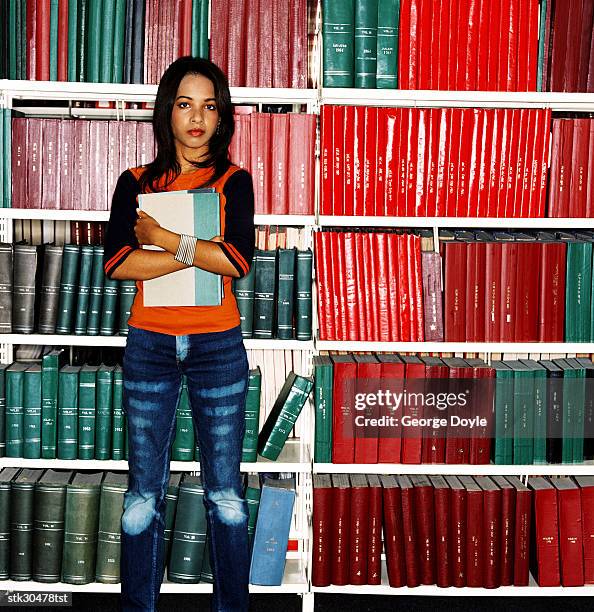 portrait of a young woman standing in a library hugging a book - cross entwicklung stock-fotos und bilder