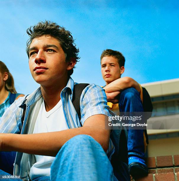 low angle close-up of two male students sitting on steps - cross-entwicklung stock-fotos und bilder