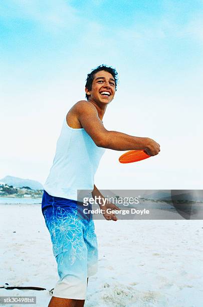 side view of a young man throwing a plastic disc at the beach - cross-entwicklung stock-fotos und bilder