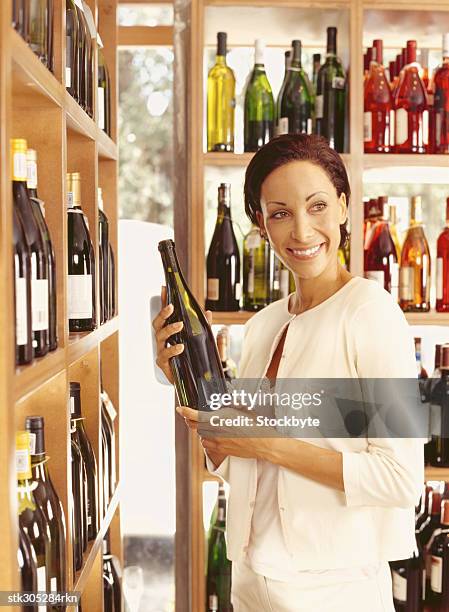 young woman holding a wine bottle in a liquor store - liquor stockfoto's en -beelden