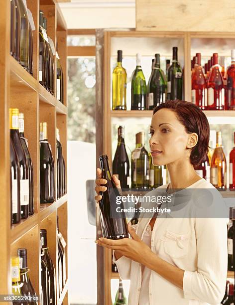 young woman holding a wine bottle in a liquor store - liquor stockfoto's en -beelden