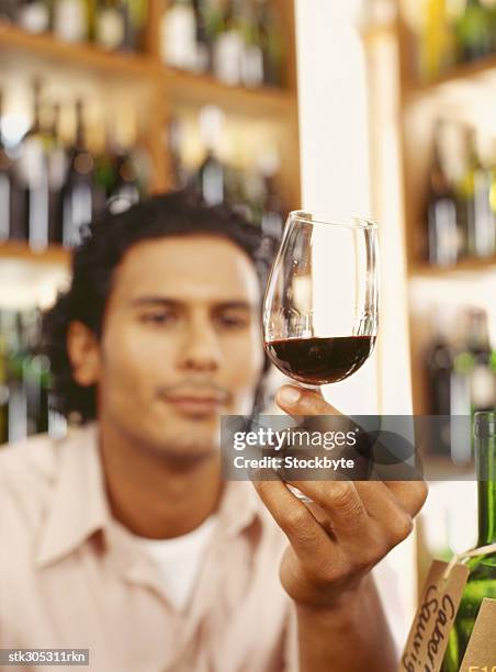 young man holding a glass of red wine in a liquor store - liquor stockfoto's en -beelden