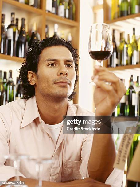 young man holding a glass of red wine in a liquor store - liquor stockfoto's en -beelden