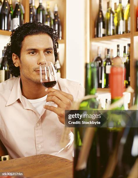 young man sniffing a glass of red wine in a liquor store - liquor stockfoto's en -beelden