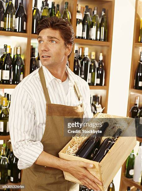 mid adult man holding a crate of wine bottles in a liquor store - liquor stockfoto's en -beelden