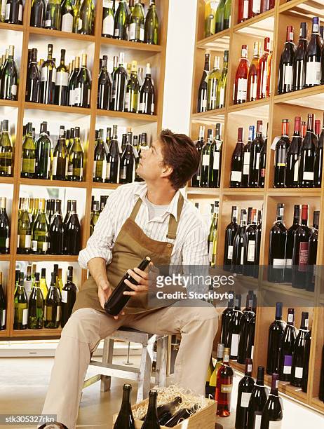 mid adult man holding a wine bottle in a liquor store - liquor stockfoto's en -beelden