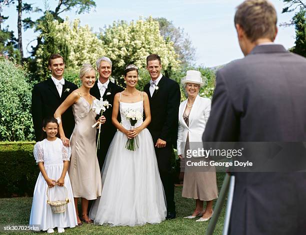 newlywed couple standing with their parents and guests and posing in front of a camera - wedding photographer stock pictures, royalty-free photos & images