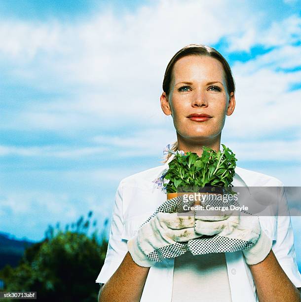 portrait of a young woman with gloves holding a potted plant - proceso cruzado fotografías e imágenes de stock