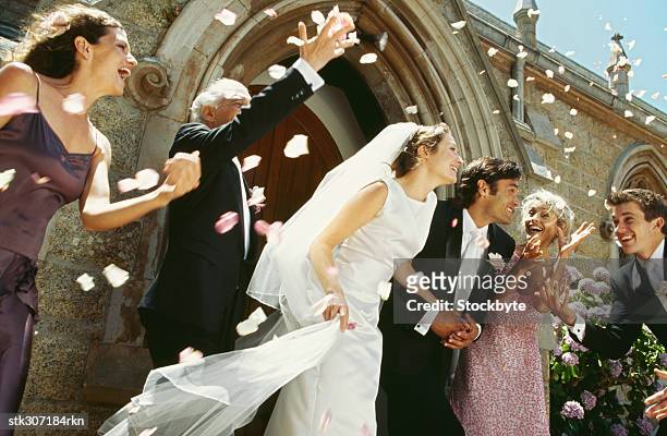 newlywed couple standing outside a church with their parents and guests - hochzeitspaar stock-fotos und bilder