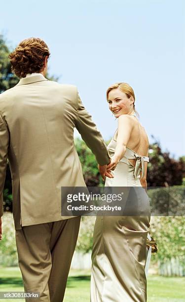 rear view of a newlywed couple holding hands and walking on a lawn - brautpaar rückenansicht stock-fotos und bilder