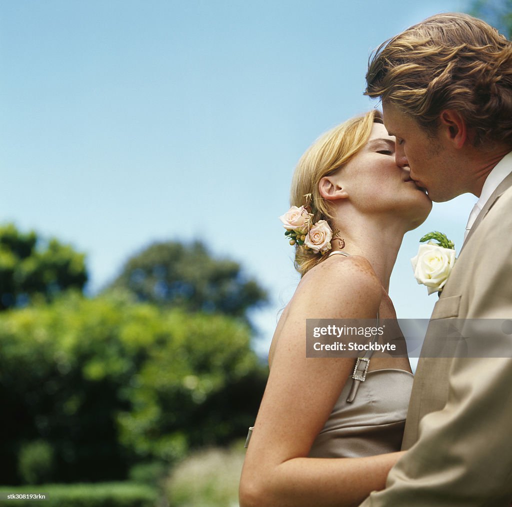 Side profile of a newlywed couple kissing in a lawn
