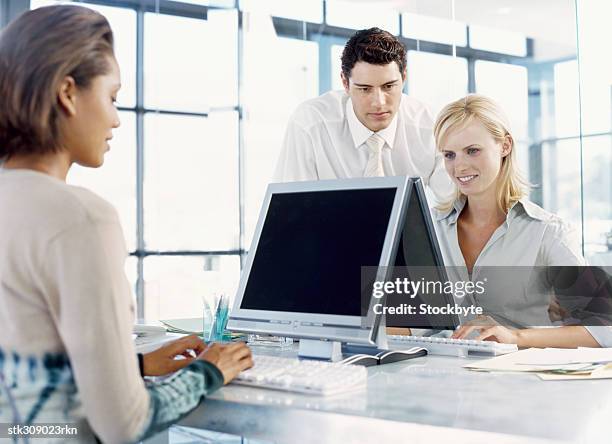 two businesswomen and a businessman sitting in front of a computer in an office - female with group of males stock pictures, royalty-free photos & images