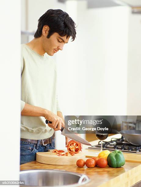 side profile of a young man cutting red bell pepper in the kitchen - bell stock-fotos und bilder