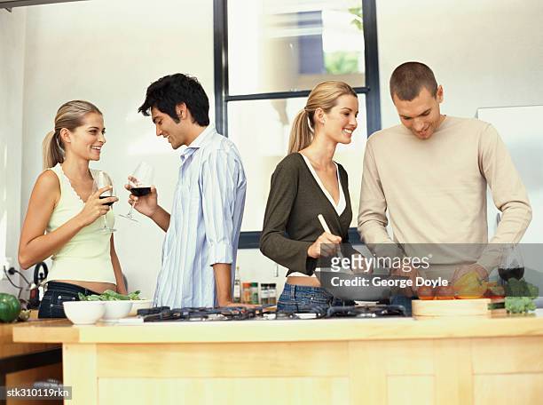 young couple cooking food with another young couple and drinking red wine in the kitchen - aother stock pictures, royalty-free photos & images