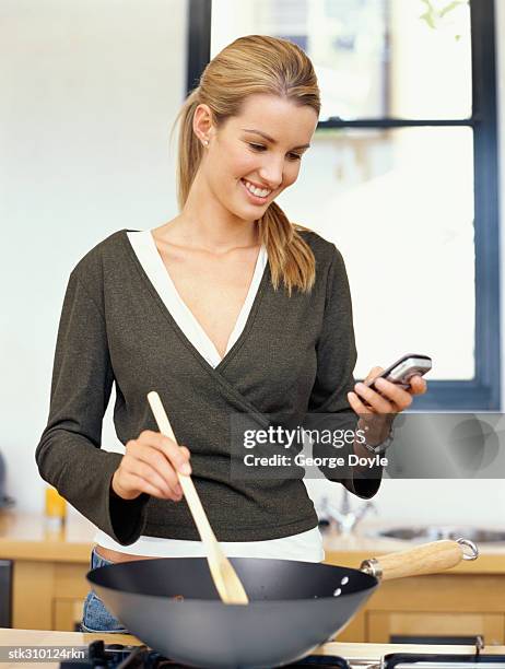 young woman cooking food and talking on a mobile phone in the kitchen - cooker dial stock pictures, royalty-free photos & images