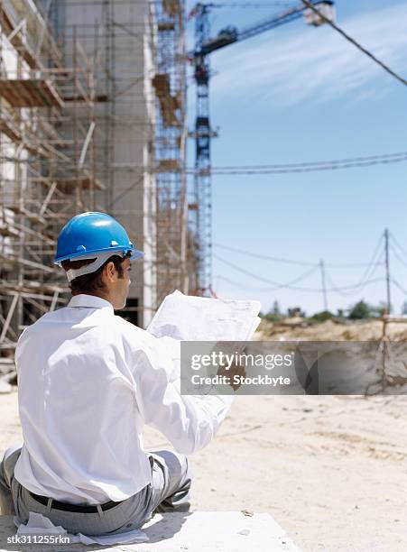 rear view of a male architect holding a blueprint - oficio de diseño fotografías e imágenes de stock