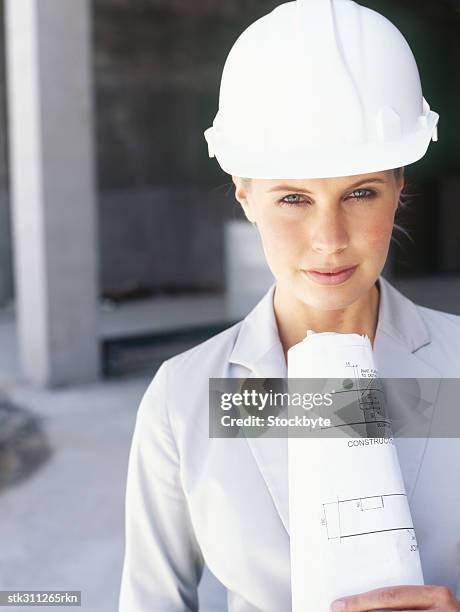portrait of a female architect holding blueprints at a construction site - trabalho de design imagens e fotografias de stock