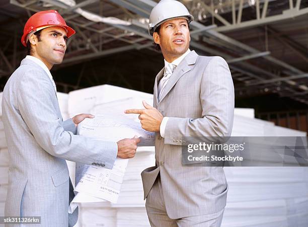 side profile of two architects holding blueprints at a construction site - design occupation stock pictures, royalty-free photos & images