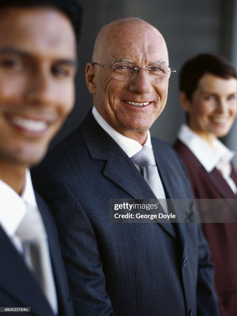 Two businessmen and a businesswoman standing in a row in an office