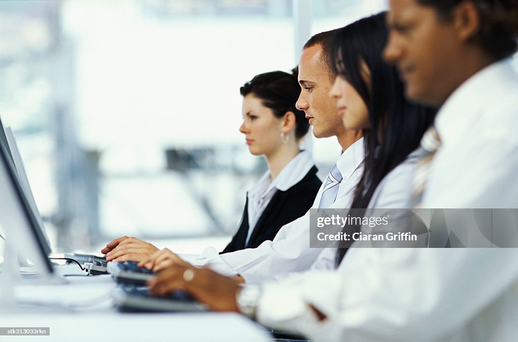 Side profile of four business executives using computers in an office