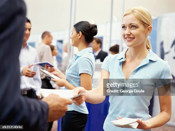 sales executives distributing brochures to business executives at an exhibition - tradeshow stock pictures, royalty-free photos & images