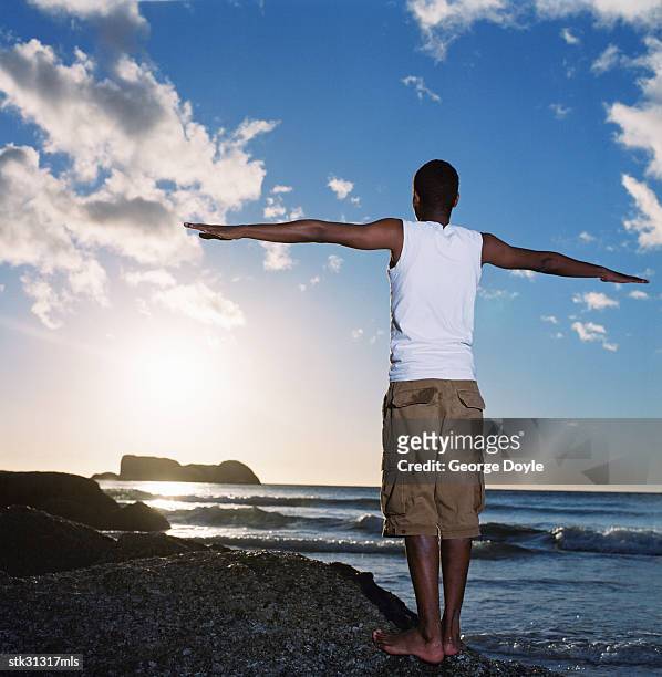 view from behind of a man standing on the beach with arms out - gestalt stock-fotos und bilder