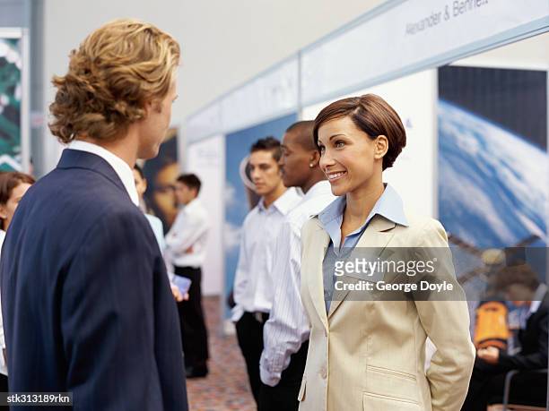 businessman and a businesswoman talking to each other at an exhibition - tradeshow stock pictures, royalty-free photos & images