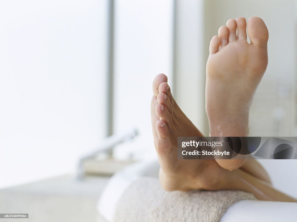 Low section view of a person's feet resting on the edge of a bathtub