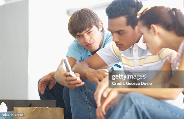 two young men and a young woman looking at a mobile phone - hand on knee stock pictures, royalty-free photos & images