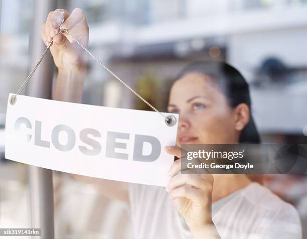 close-up of a young woman hanging closed sign on a glass door - door stockfoto's en -beelden