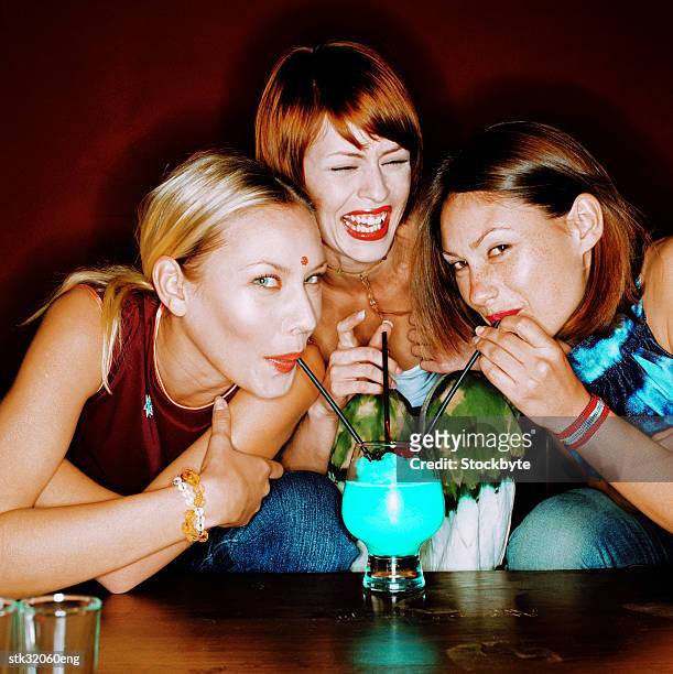 portrait of three women drinking with straws from a single cocktail in a bar - bar ストックフォトと画像