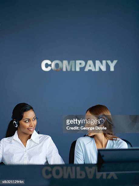 two businesswomen wearing handsets and talking in an office - communication occupation stock pictures, royalty-free photos & images