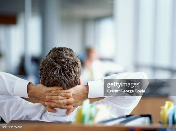 rear view of a businessman relaxing with his hands behind head in an office - stretching hands behind head rear view stock-fotos und bilder